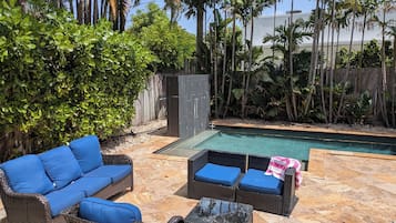 A poolside area with wicker furniture, a pool, and tropical plants.