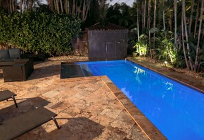 A swimming pool with a tiled deck, surrounded by greenery and a small wooden structure. - #1 Family Oasis/Htd SW Pool/3BR/10mins to all/No Car Rqd/New Pics/All Updated (Fort Lauderdale)