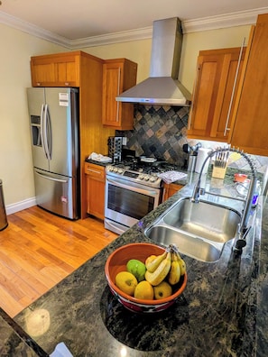 A kitchen with wooden cabinets, a stainless steel refrigerator, an oven, a stove, and a bowl of fruit on the counter.