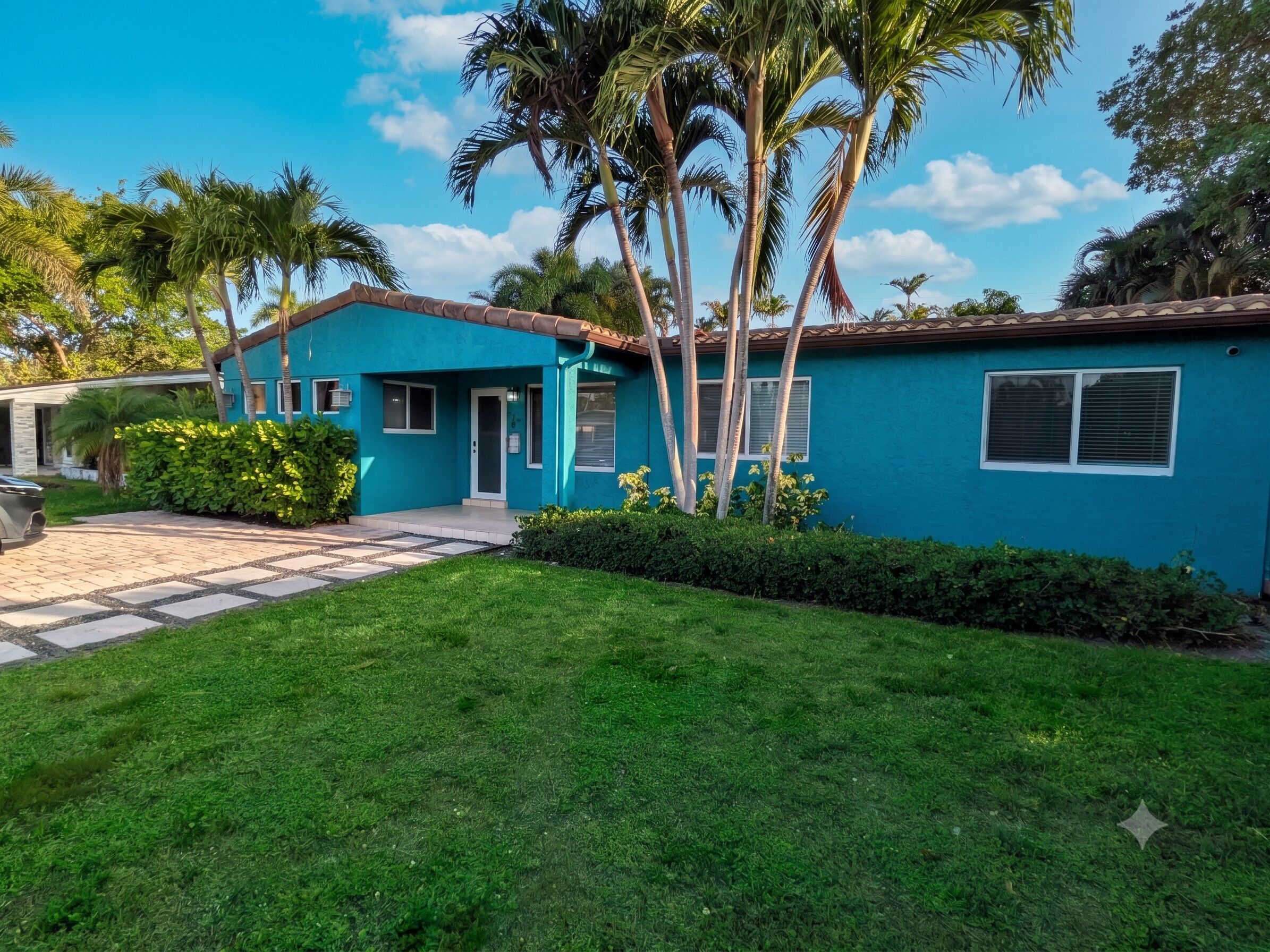 A blue house with a tiled driveway, palm trees, and a well-maintained lawn.