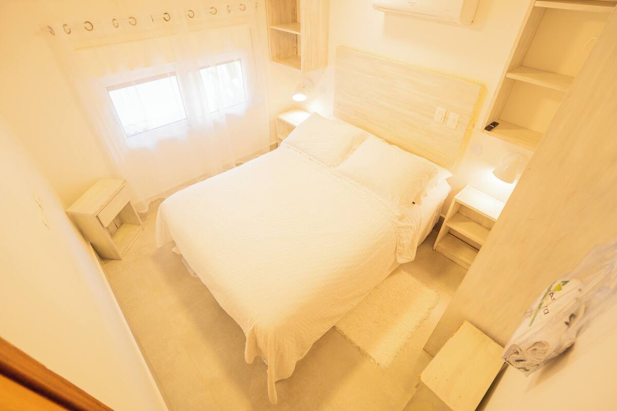 Un lit blanc, bien fait, avec une tête de lit, une table de chevet et une petite table de nuit.