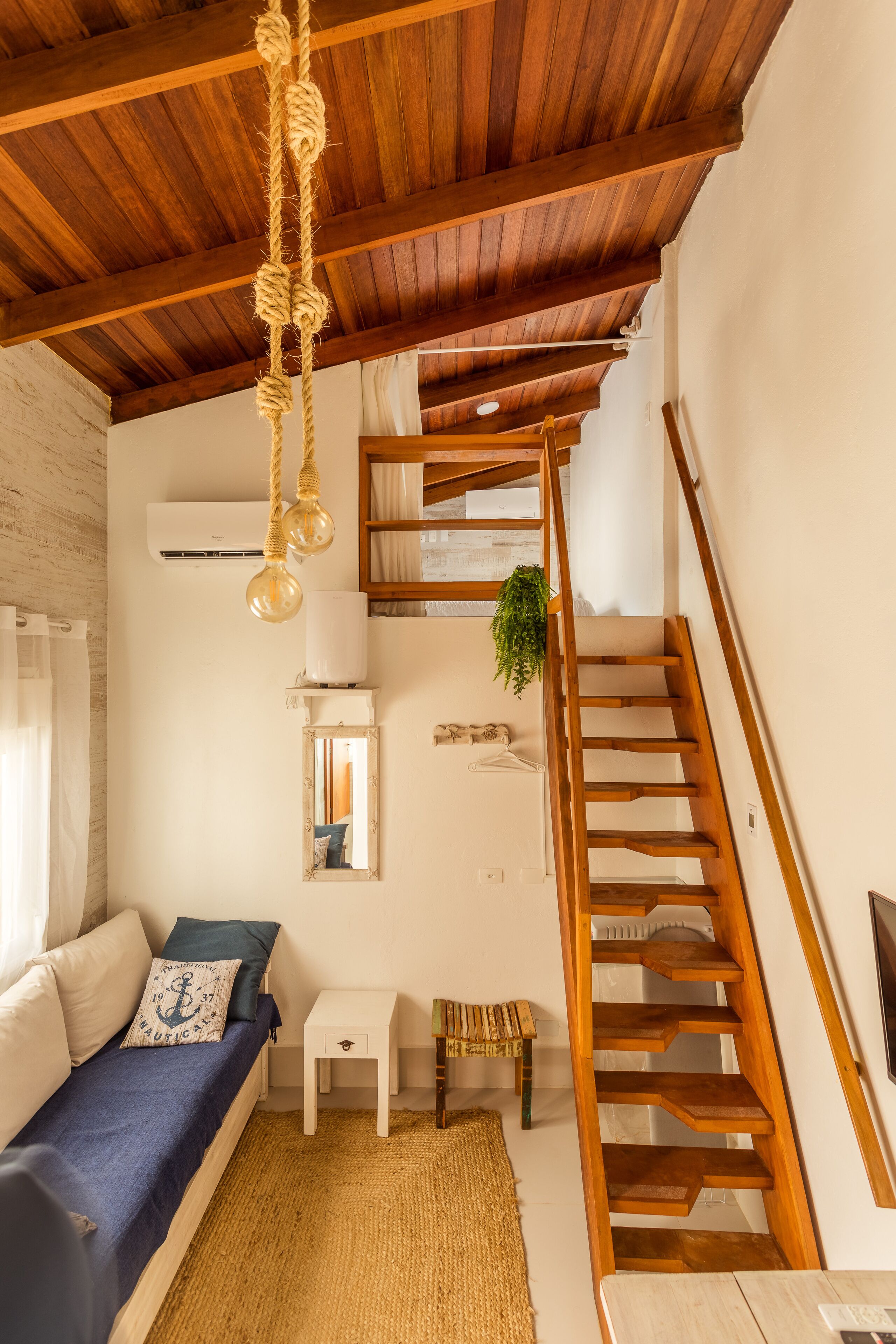 Una habitación acogedora con una escalera de madera, una mesita, un banco y una lámpara colgante.
