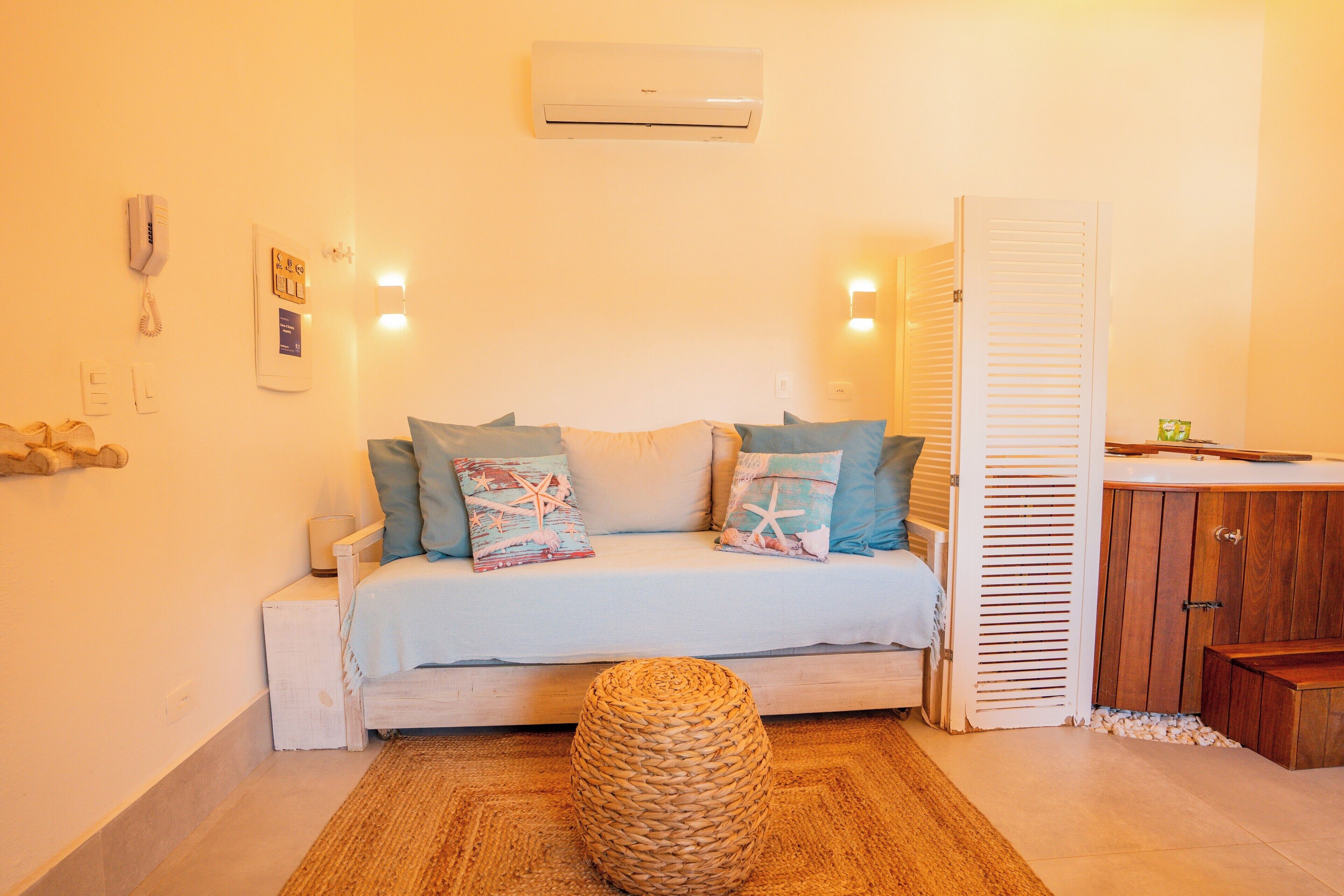 A bedroom with a bed, bedside table, and a small round woven stool.