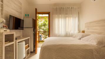 A bedroom with a bed, a TV, a refrigerator, and a balcony with a view of greenery.