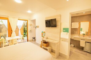 Une chambre d’hôtel comprenant un lit, un téléviseur fixé au mur, une petite table avec des chaises, une fenêtre avec des rideaux et une salle de bain avec un miroir et un lavabo.