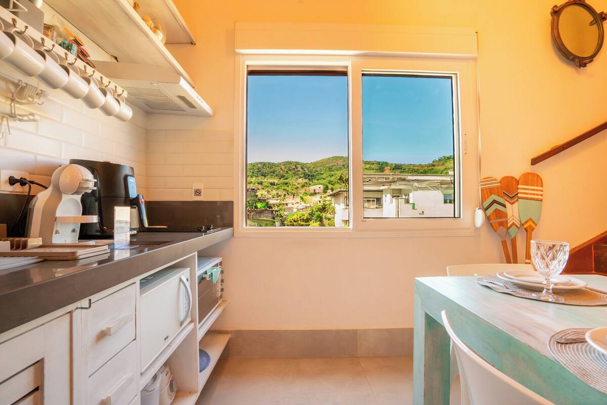 Une cuisine donnant sur un paysage vallonné grâce à une fenêtre, un coin repas avec une table mise pour deux personnes, et un miroir fixé au mur.