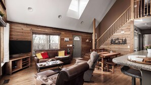 Un salón espacioso con un televisor grande, paredes de madera, una escalera y un comedor.