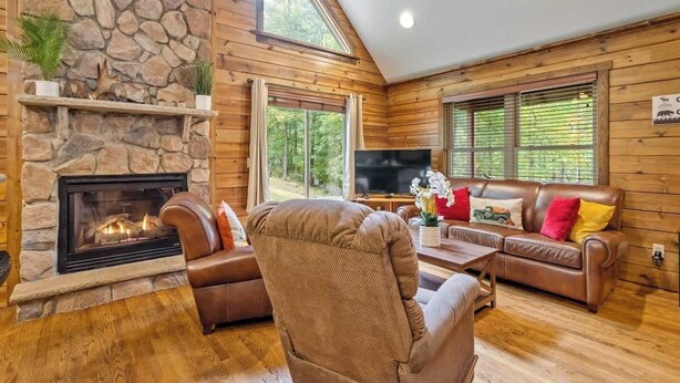 Una sala de estar acogedora con chimenea de piedra, sofás de cuero y un televisor grande.