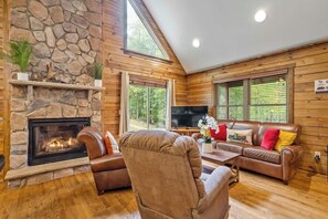 A cozy living room with a stone fireplace, leather sofas, and a large TV.