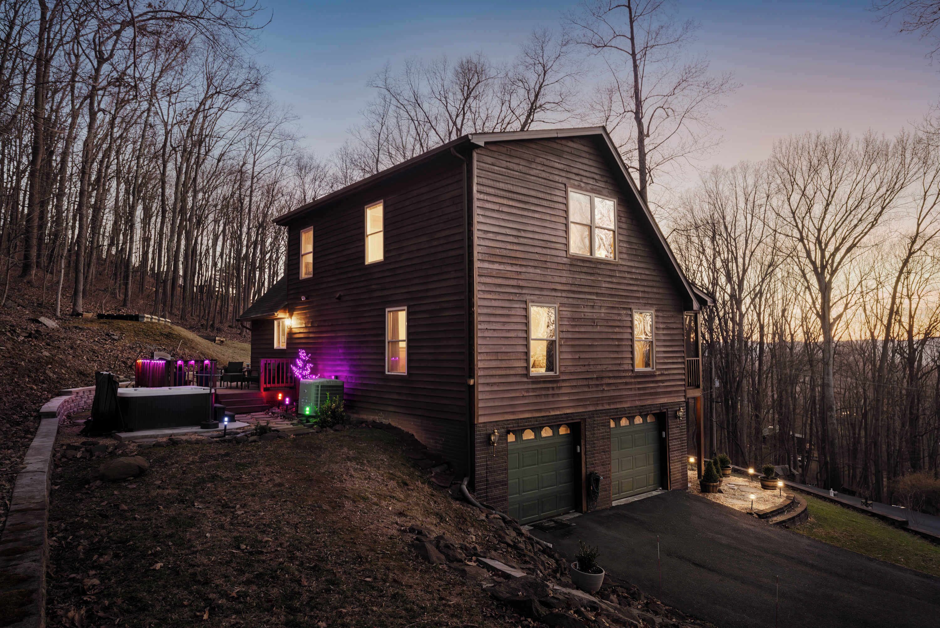 A two-story house with a dark wooden exterior, a front porch, and a driveway leading to a garage.