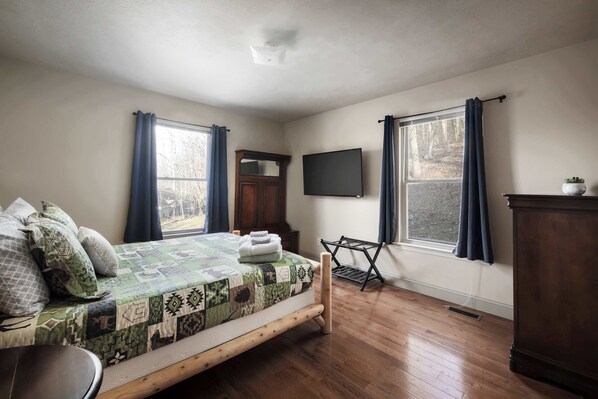 A bedroom with a wooden bed, a flat-screen TV, a dresser, and a window with curtains.