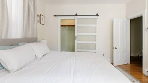 A bedroom with a bed, a wardrobe with a sliding door, and a door leading to another room. - Charming 2 bedroom near Central Square!  (Cambridge)