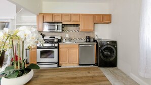A compact kitchen with wooden cabinets, a microwave, stove, oven, dishwasher, and a washing machine. - Charming 2 bedroom near Central Square!  (Cambridge)