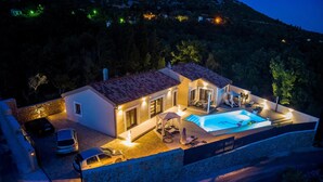 Una villa moderna con piscina, pareti in pietra e un'auto parcheggiata davanti.