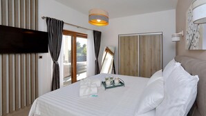 Una camera d'albergo con un letto, una TV, una finestra con tende, un armadio in legno e una lampada a parete.