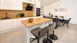 Una cucina moderna con mobili bianchi, un piano di lavoro in legno e un forno integrato. Sono presenti sgabelli da bar e un tavolo da pranzo con sedie.