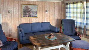 A room with a wooden paneled wall, a blue sofa, a matching armchair, a wooden coffee table, and a plaid curtain. - 3 bedroom awesome home in Vikersund (Vikersund)