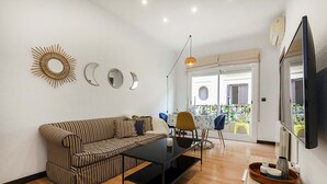A living room with a striped sofa, a glass coffee table, a TV, and a dining area with chairs and a table.
