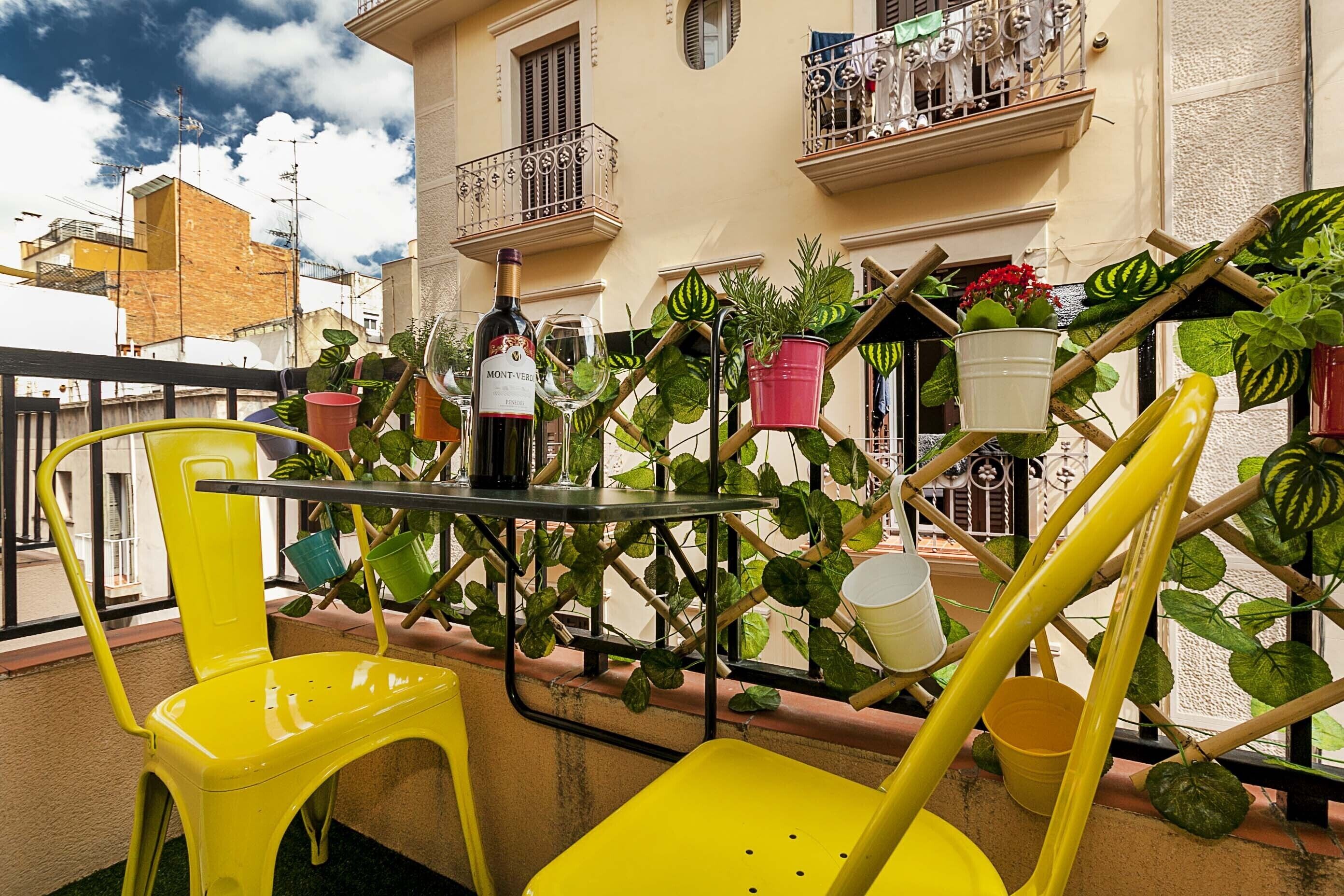 Un balcón con sillas amarillas, una mesa y varias plantas en macetas.