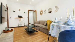 A modern living room with a sofa, a dining table set, and a TV mounted on the wall.