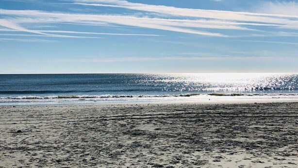 Ein Strand mit klarem Himmel und Sonnenlicht, das sich auf dem Wasser spiegelt.