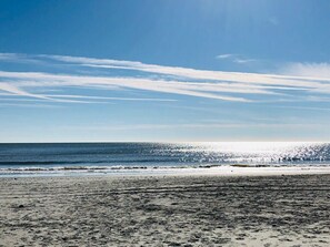 Uma praia com céu claro e o sol refletindo na água.