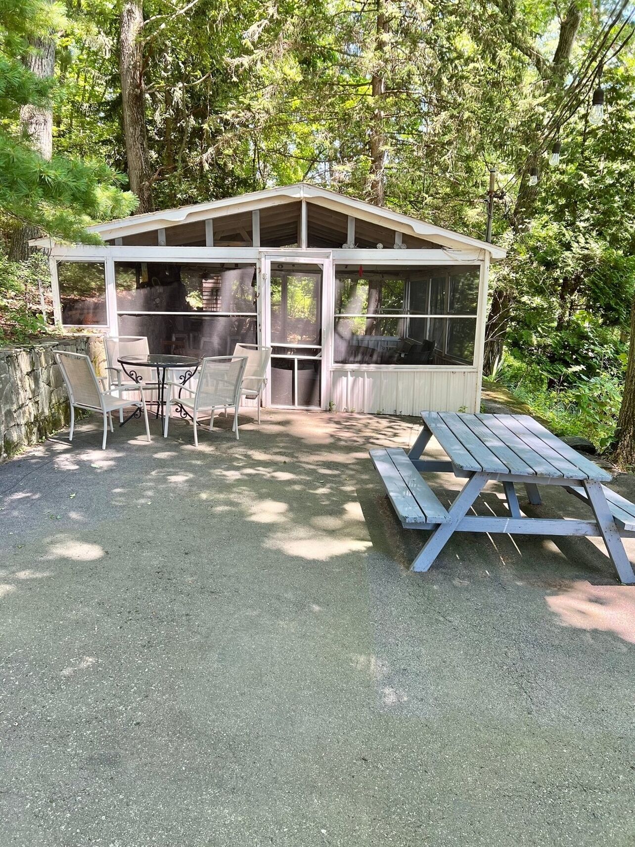 Et overdækket udendørs opholdsområde med borde, stole, et picnicbord og en grill.