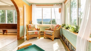 Ein Zimmer mit Pooltisch, zwei Korbstühlen, einer Bank und Blick auf Grün durch große Fenster.