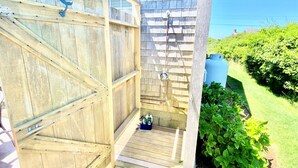 A wooden outdoor shower area with a wooden deck, a water tank, and lush greenery.