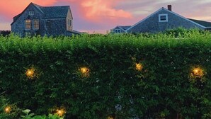 A house with a stone exterior and a sloped roof, surrounded by a well-maintained hedge with string lights.