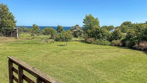 Eine grüne Wiese mit einer Holzbank, Bäumen und Blick auf den Ozean.