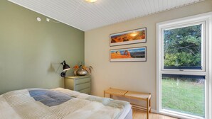 Ein Schlafzimmer mit einem Bett, einem Nachttisch mit Lampe, einer Bank und zwei gerahmten Bildern an der Wand.