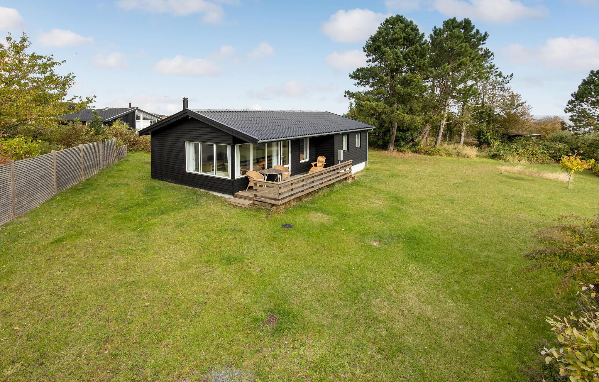 A black house with a porch and a small deck, surrounded by a grassy yard and trees.
