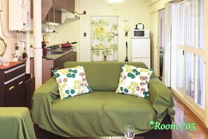 Quarto com sofá, mesa de jantar, cozinha e janela com cortinas.