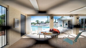 A poolside area with a table and chairs, a covered seating area, and a view of the pool and surrounding landscape.