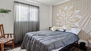 Une chambre à coucher comprenant un lit, une chaise, une fenêtre avec des rideaux, une tapisserie et un ventilateur de plafond.