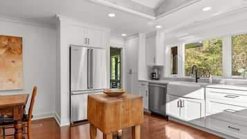 Une cuisine moderne avec des meubles blancs, des appareils en acier inoxydable et un tabouret en bois.