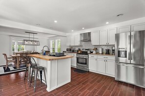 A modern kitchen with white cabinets, stainless steel appliances, a central island, and a dining area with wooden chairs.