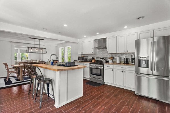 A modern kitchen with white cabinets, stainless steel appliances, a central island, and a dining area with wooden chairs.