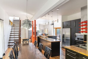 Une cuisine moderne dotée d’un îlot central, d’appareils électroménagers en acier inoxydable et d’un coin repas avec une longue table et des chaises en bois.
