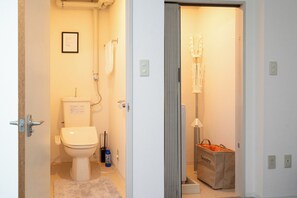 Une salle de bain avec des toilettes, un panneau encadré accroché au mur, un porte-serviettes, une lampe sur pied et un sac à linge.