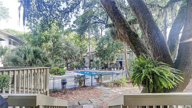 Zona de piscina envoltada d'arbres i un edifici amb balcons.