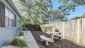 Ein Garten mit Holzzaun, einem Betonweg und einem kleinen Tisch mit Bänken.