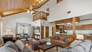 A spacious living area with a high ceiling, wooden beams, and a kitchen with wooden cabinets. - Lakefront Estate • Sleeps 23 • Firepit & Kayaks (Seguin)