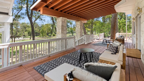 A covered outdoor area with a wooden deck, stone pillars, a white railing, and a seating area with a sofa, table, and chairs. - Lakefront Estate • Sleeps 23 • Firepit & Kayaks (Seguin)
