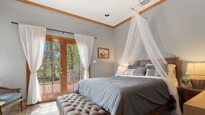 A bedroom with a large bed, a bench, a nightstand, and a window with curtains. - Lakefront Estate • Sleeps 23 • Firepit & Kayaks (Seguin)