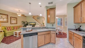 A modern kitchen with wooden cabinets, a built-in dishwasher, and a dining area with a white table and chairs.