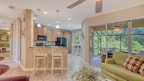 A modern kitchen with a central island, bar stools, and a dining area with a view of the outdoors.