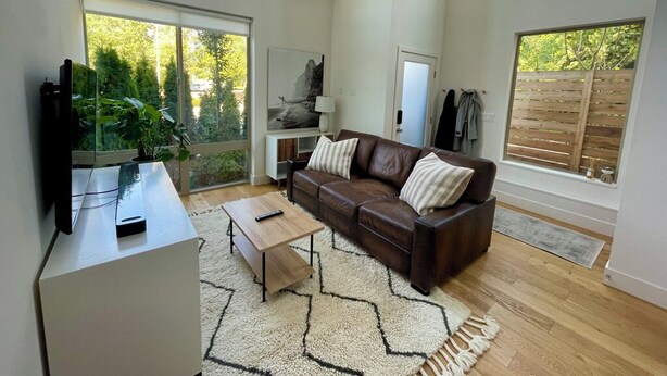 Ein geräumiges Wohnzimmer mit einer braunen Ledersofa, einem Couchtisch und einem großen Fenster mit Blick auf Grünfläche.