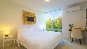 Ein Schlafzimmer mit Bett, Nachttisch, Stuhl und einem Fenster mit Blick auf Bäume.
